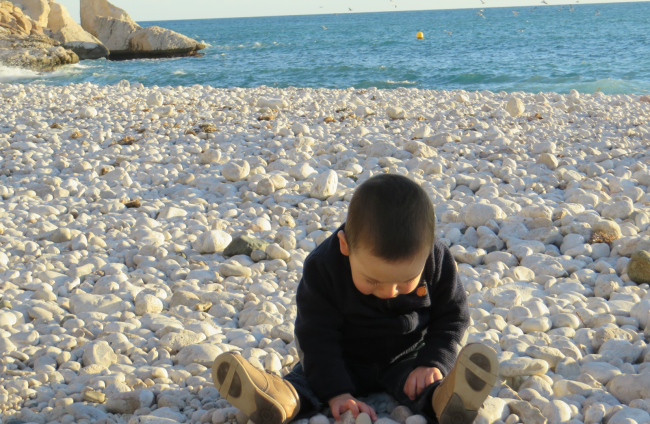 Un niño juega con piedras en la playa. ECB