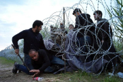 Refugiados sirios cruzan la alambrada de espino situada por las autoridades húngaras en su frontera.-Bela Szandelszky/AP/BEA SZANDELSKY