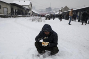 Un refugiado come en medio de la nieve en Belgrado.-REUTERS / MARKO DJURICA