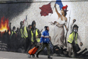 Un hombre pasa junto a un mural que reproduce una versión de La libertad guiando al pueblo, de Eugene Delacroix, con la presencia de chalecos amarillos, idea del artista Pascal Boyart.-GETTY IMAGES