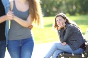 Una chica sentada en el parque siente envidia al ver a una pareja.-123RF