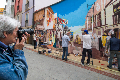 Un hombre hace una fotografía al mural mientras los artistas trabajan en él. TOMÁS ALONSO