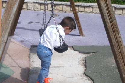 Un niño juega en un columpio con el suelo roto.-L. VELÁZQUEZ