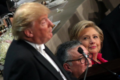 Clinton, sentada junto al obispo de Nueva York, observa a Trump durante su intervención en la cena benéfica del jueves.-REUTERS / CARLOS BARRIA