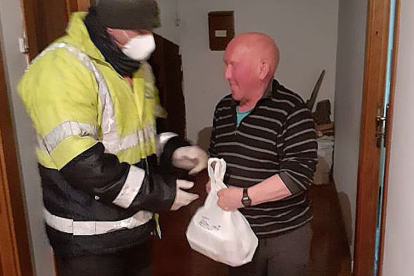 Un voluntario protegido con mascarilla y guantes entrega comida a un hombre mayor en Quintanar de la Sierra. ECB