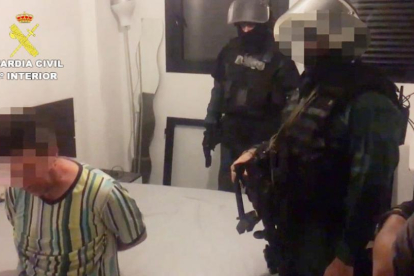 Dos agentes vigilan de la Guardia Civil vigilan a uno de los detenidos en su domicilio, ubicado en Zaragoza.-GUARDIA CIVIL