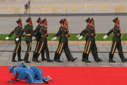 Dos trabajadoras limpian una alfombra roja ante un grupo de soldados, este lunes en Tiananmén.-EFE