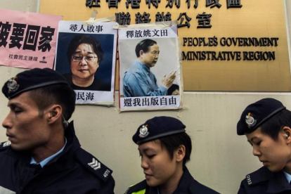 Unos policías frente a las fotos de Gui Minhai (izquierda) y otro de los cinco libreros, Yau Wentian, que fue condenado a 10 años de prisión en el 2015.-AFP / ANTHONY WALLACE