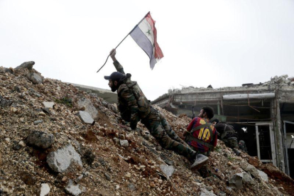 Un soldado del régimen sirio coloca una bandera en una zona de combate.-HASSÁN AMMAR / AP