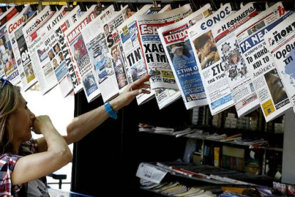 Una mujer mira con curiosidad y cierto temor la oferta informativa de la prensa griega.-Foto: AP / PETROS KRADJIAS