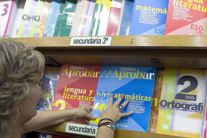 Una mujer ordena los libros de texto por cursos en las estanterías.
