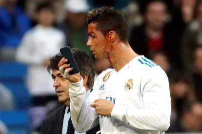 Cristiano abandona el césped del Bernabéu mirándose la brecha en la ceja en el móvil del médico.-EFE / JUAN CARLOS HIDALGO