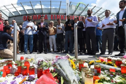 Varias personas rezan en el memorial de velas y flores, colocada frente al centro comercial Olympia, en Munich, este domingo.-AFP / CHRISTOF STACHE