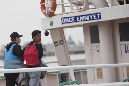 Un migrante pakistaní mira hacia atrás, conducido por un funcionario, en el ferri a punto de partir hacia Turquía, en Lesbos, este viernes.-AP / PETROS GIANNAKOURIS