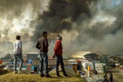 Inmigrantes observan el campamento evacuado de Calais con parte de las barracas ardiendo.-AFP / PHILIPPE HUGUEN