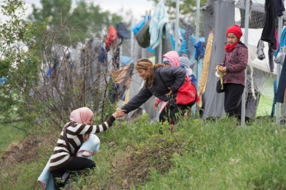 Una refugiada con su bebé en brazos, ayudada por otra a subir una colina en un campo cerca de Idomeni (Grecia), este miércoles.-AFP / TOBIAS SCHWARZ