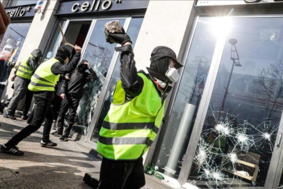 Un chaleco amarillo rompe el cristal de una tienda en los Campos Elíseos de París.-GEOFFROY VAN DER HASSELT (AFP)