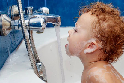 Un niño trata de beber agua del grifo  de la bañera.-EL MUNDO