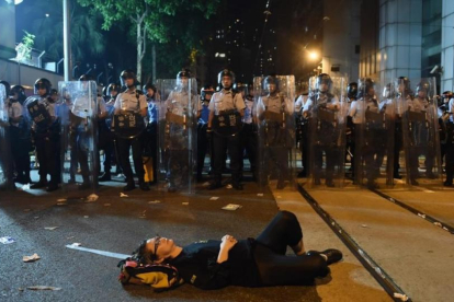 Una manifestante estirada en el suelo bloquea una de las calles de Hong Kong frente a una fila de policías.-AFP / ANTHONY WALLACE