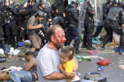 Un refugiado sirio con un niño en brazos en los disturbios de Röszke, en la frontera entre Serbia y Hungría en septiembre del 2015.-KARNOK CSABA