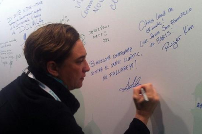 Colau firma en una pizarra su compromiso contra el cambio climático, en París, este viernes.-EL PERIÓDICO