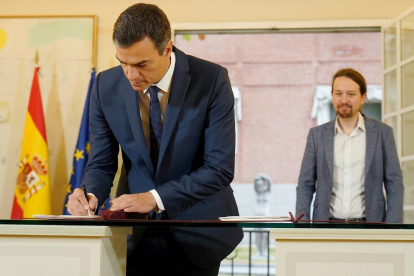 Pedro Sánchez firma el acuerdo presupuestario ante la mirada de Pablo Iglesias, en la Moncloa-JOSÉ LUIS ROCA