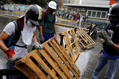 Unos manifestantes levantan una barricada en Caracas.-REUTERS / CARLOS GARCIA RAWLINS