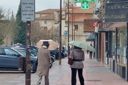 Dos mujeres se protegen de la lluvia con sendos paraguas, ayer en la calle Calzadas. L. G. L.