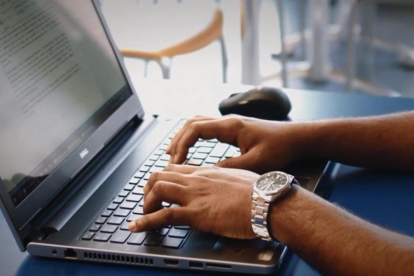 Un hombre escribe en un ordenador portátil.-