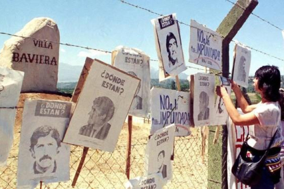 Una mujer cuelga carteles de chilenos desaparecidos en la cerca de Colonia Dignidad, que sirvió de centro de tortura de Pinochet.-REUTERS