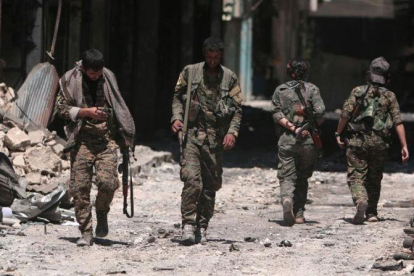 Combatientes de las Fuerzas Democráticas de Siria caminan sobre los escombros de tiendas y edificios dañados por la batalla en la ciudad de Manbij.-RODI SAID (REUTERS)