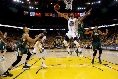 El jugador de los Warriors de Golden State Stephen Curry (c) entra a canasta a pesar de la defensa de Boris Diaw (2º dcha) y Rudy Gobert (dcha).-EFE