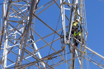 Dos trabajadores aseguran la cruceta que se ha quedado colgada de la torre eléctrica.