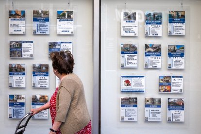 Una mujer se fija en los anuncios de inmuebles en el escaparate de una inmobiliaria de Burgos.