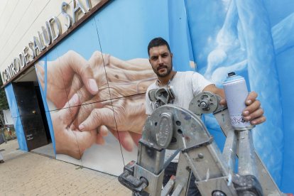 Christian Saldaña posa ante el espectacular mural que está rematando en el centro de Salud de Santa Clara. FOTOS: © ECB / SANTI OTERO