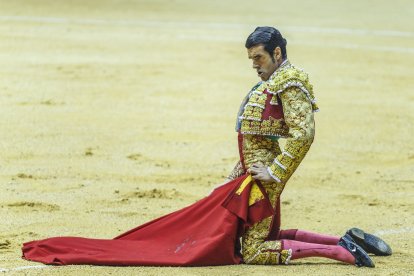 De rodillas, con gesto de concentración.