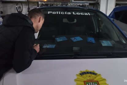 Un agente de la Policía Local estudian las características de distintas tarjetas sobre un salpicadero de un coche oficial.
