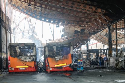 Dos trabajadores contemplan los restos de dos buses alcanzados por las llamas.