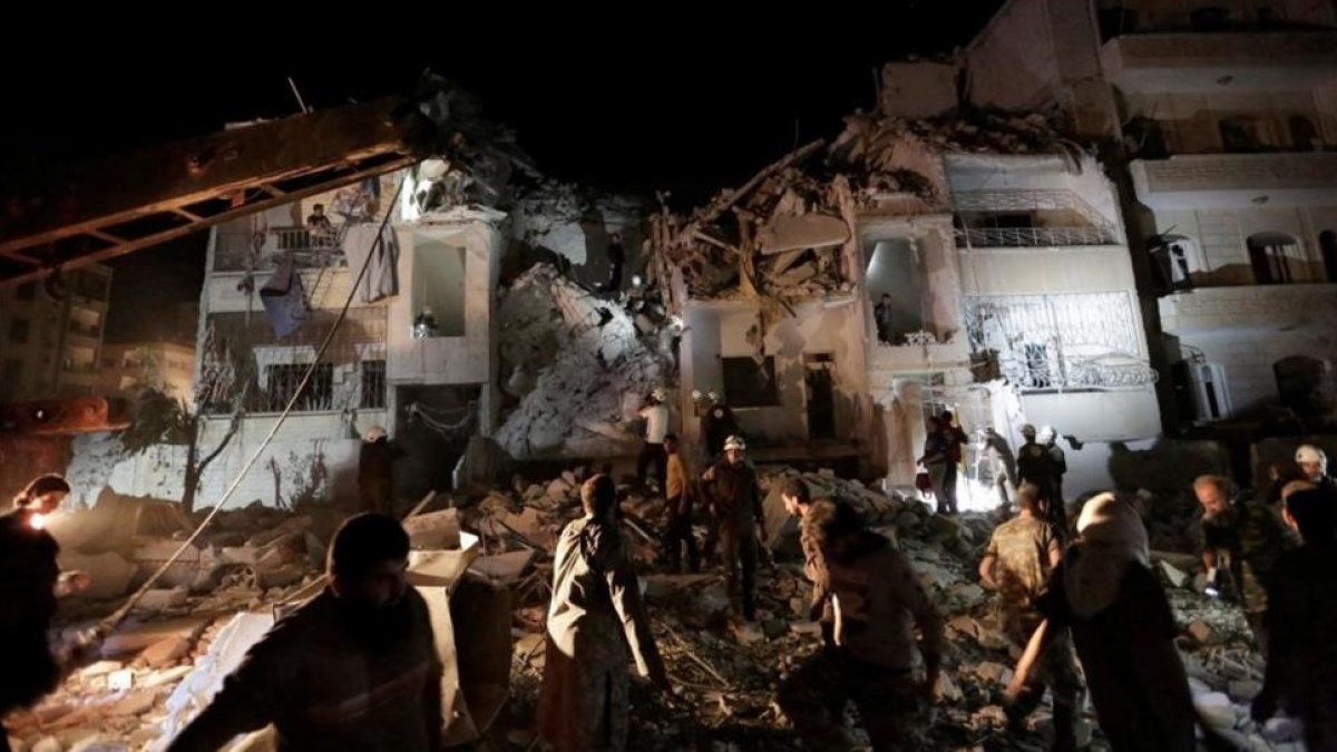 Civiles y miembros de la defensa civil buscan supervivientes en un edificio destrozado por los bombardeos aéreos, este lunes por la noche, en Idleb.-REUTERS / KHALIL ASHAWI