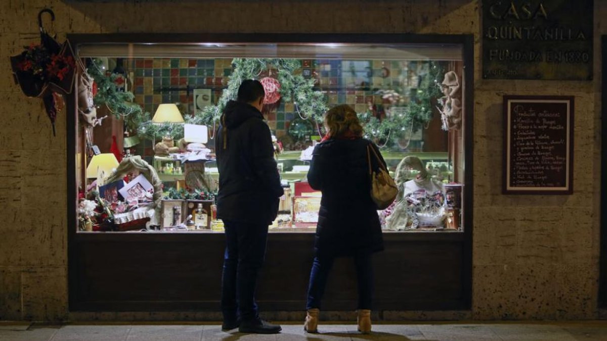 Dos personas observan el escaparate de una tienda de alimentación decorado ya con motivos navideños y artículos típicos de estas fiestas.-RAÚL G. OCHOA