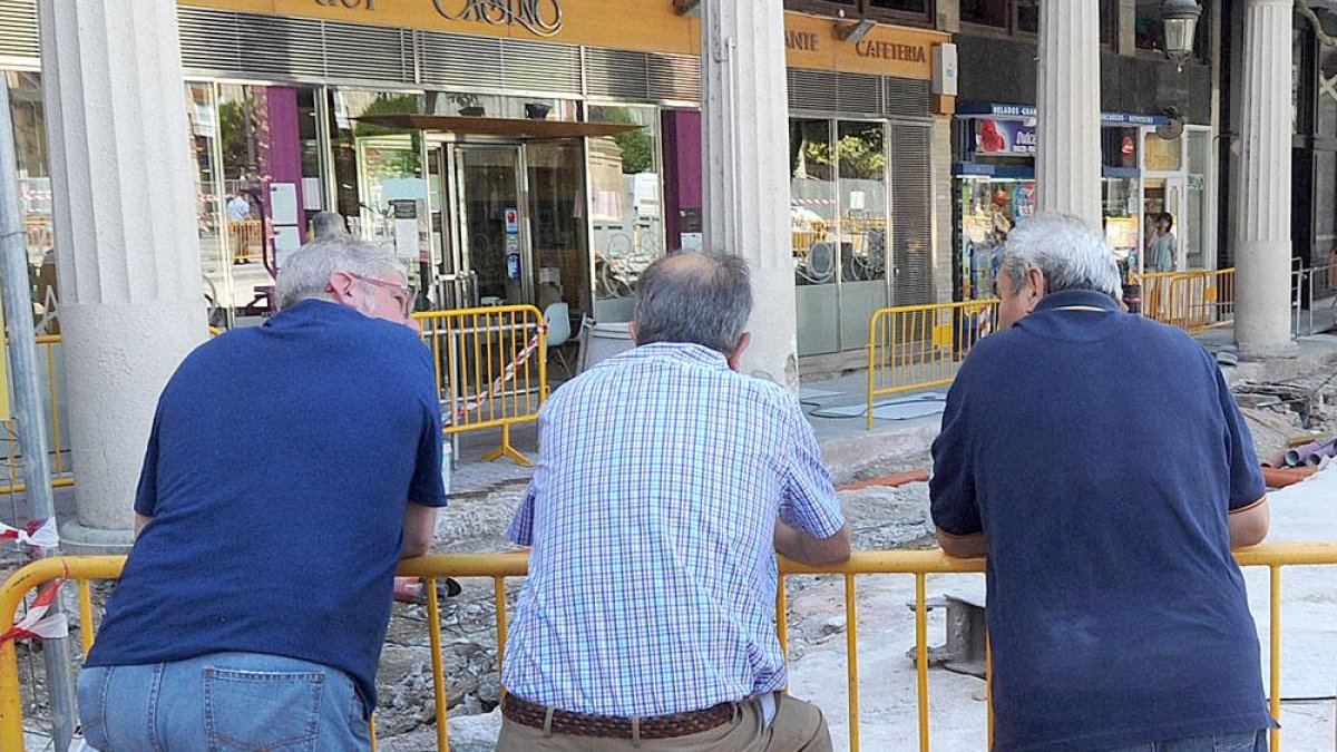 Tres hombres mayores conversan mientras observan una obra apoyados en una valla metálica.-ISRAEL L. MURILLO