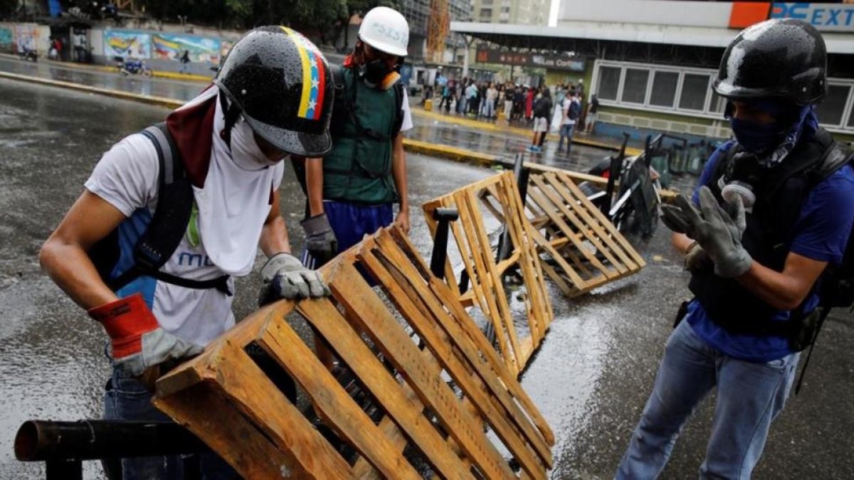 Unos manifestantes levantan una barricada en Caracas.-REUTERS / CARLOS GARCIA RAWLINS