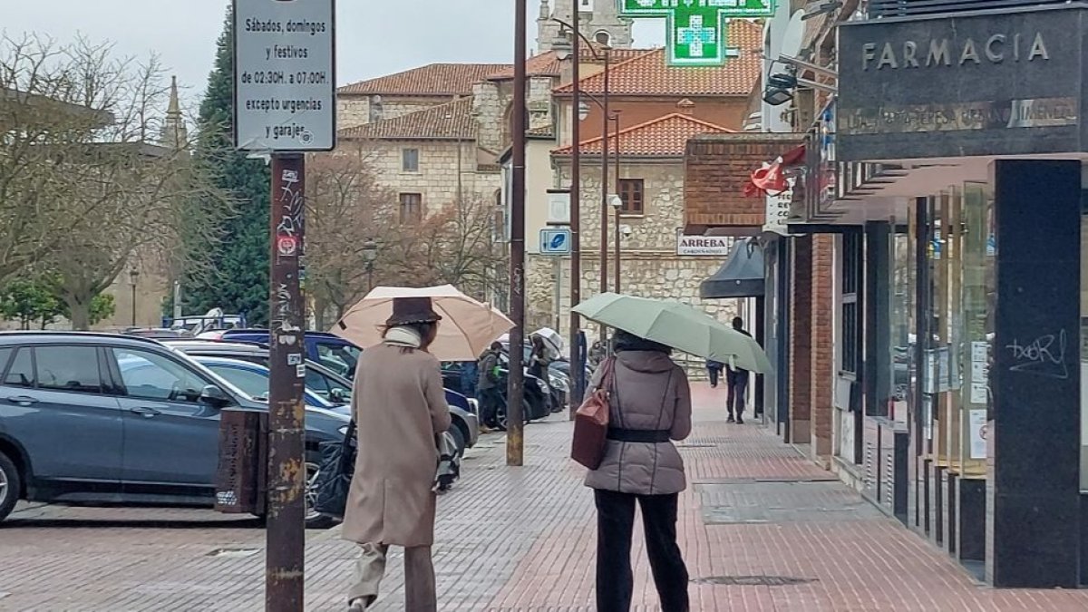 Dos mujeres se protegen de la lluvia con sendos paraguas, ayer en la calle Calzadas. L. G. L.
