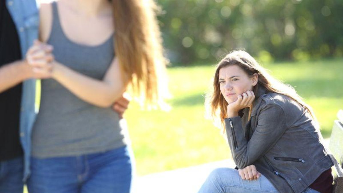 Una chica sentada en el parque siente envidia al ver a una pareja.-123RF