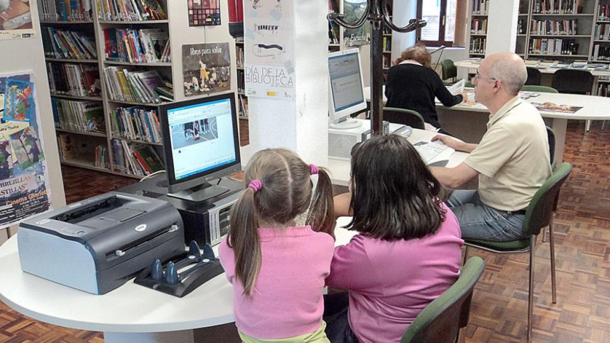 Dos niñas y un adulto navegan en internet en la biblioteca pública de Pradoluengo.-ECB