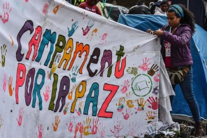 Una joven ayuda a colocar una pancarta a favor del acuerdo de paz en la acampada de la plaza Bolivar, en Bogotá.-AFP / LUIS ACOSTA