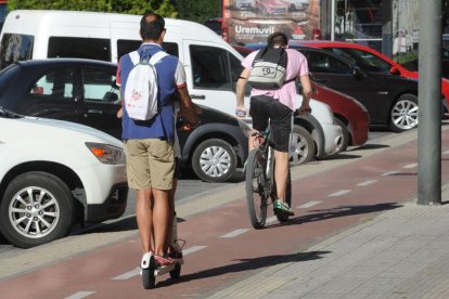 Un hombre en patinete eléctrico compartiendo con un ciclista el carril bici.