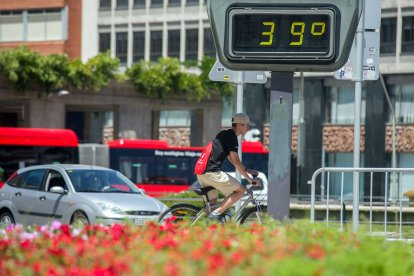 Un ciclista y varios coches pasan junto a un termómetro a 39ºC en Burgos capital.