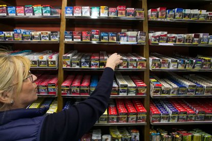 La dependienta de un estanco coge una cajetilla de tabaco del casillero de venta del establecimiento.