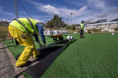 Dos operarios ajustan el nuevo césped artificial del campo de fútbol siete del complejo deportivo José Luis Talamillo.